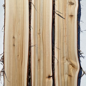 May include: Three pieces of wood with a natural wood grain pattern. The wood is light brown with darker brown streaks. The wood is smooth and has a slightly rough texture.