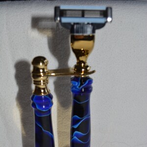 May include: A gold-colored stand with two blue and black handles, holding a razor with a blue and silver blade.