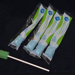 May include: Four individually wrapped oral swabs for professional oral hygiene. The swabs are packaged in clear plastic with green and white labeling that reads "Unflavored Oral Swabs for Professional Oral Hygiene". A white swab stick with a green sponge tip is also pictured.