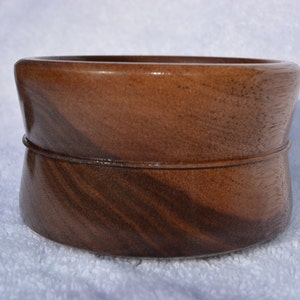 Puede incluir: Un cuenco de madera marrón oscuro con un borde ligeramente acampanado y un sutil patrón de remolino en la veta de la madera.