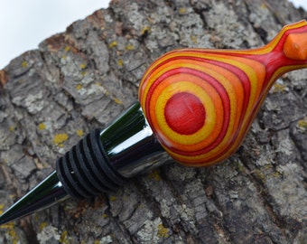 May include: A red, yellow, and orange wooden bottle stopper with a silver metal base. The stopper is shaped like a teardrop and has a swirling pattern.