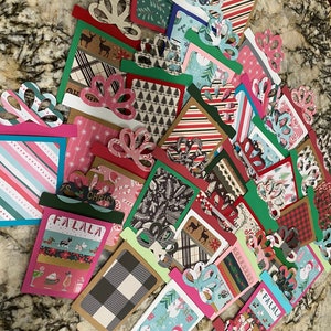 May include: A collection of Christmas-themed gift card holders featuring various patterns and designs, including plaid, snowflakes, and reindeer. The holders are made of paper and have a festive, handmade look.