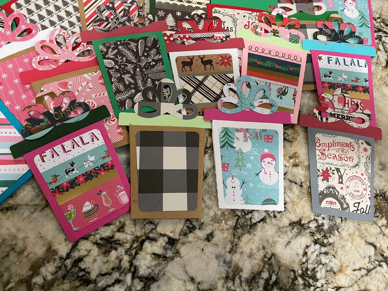 May include: A collection of handmade Christmas gift tags featuring various holiday designs, including snowmen, plaid patterns, and the words "Falala" and "Compliments of the Season".