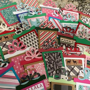 May include: A collection of colorful Christmas gift tags with various festive patterns and designs. The tags are made of paper and have a bow shape at the top. Some of the tags have text on them, such as "Merry Christmas" and "Happy Holidays".