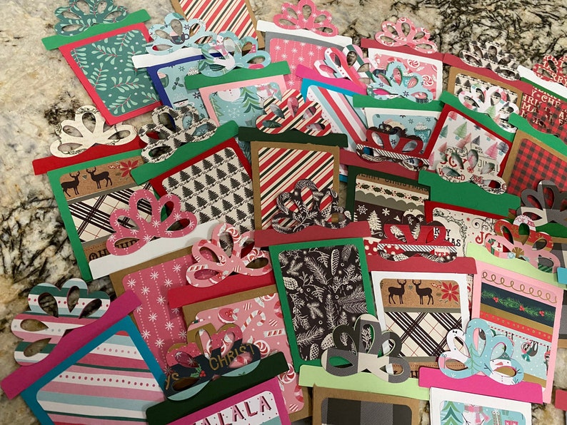 May include: A collection of colorful Christmas gift tags with various festive patterns and designs. The tags are made of paper and have a bow shape at the top. Some of the tags have text on them, such as "Merry Christmas" and "Happy Holidays".