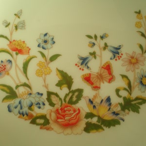 May include: A white ceramic plate with a floral design featuring a butterfly, flowers, and leaves in shades of blue, red, yellow, and green.