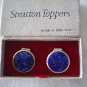 May include: A pair of round Stratton Toppers in a white box with the text Stratton Toppers and Made in England. The circular items feature a deep blue mottled surface with gold-colored flecks and a ribbed gold-tone metal border, set in red.