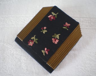 May include: A small, black fabric box with a gold trim and floral embroidery. The flowers are pink and green.