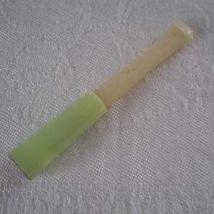 May include: A bottle stopper in pale yellow and light green. The base is light green, and the handle is pale yellow. The object is on a white, textured surface.