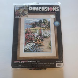 May include: A Dimensions needlepoint kit titled "Summer Sublime" designed by Erin Dertner. The kit includes a framed canvas with a scenic landscape of a garden path leading to a coastal view. The canvas measures 16" x 20" (41 x 51 cm).