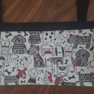 May include: A rectangular tote bag with black straps and a black border. The bag features a white background with a repeating pattern of various cartoon dogs in gray, red, and black, along with bone illustrations.