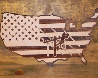 May include: A wooden cutout of the United States of America with an American flag design and a silhouette of a lineman working on a power line.