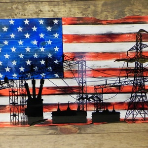 May include: A distressed wood American flag with a silhouette of an electrical power grid and transformers. The flag is painted in red, white, and blue.