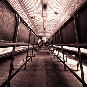 Puede incluir: Una fotografía en blanco y negro de un vagón de tren vacío con filas de asientos enfrentados. Los asientos son de metal y tienen un aspecto desgastado y vintage.