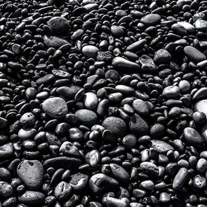 May include: A close-up image of a large collection of smooth, black river rocks. The rocks are various sizes and shapes, and they are all wet and glistening.