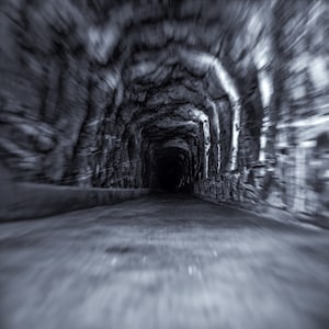Puede incluir: Una foto en blanco y negro de un túnel oscuro con una superficie de piedra rugosa. El túnel está iluminado por una luz tenue al final.