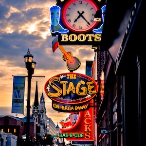 Op de afbeelding: Een neonbord met de woorden "Big Time Boots" en een klok. Onder het bord is een ander neonbord met de tekst "The Stage on Broadway". Er is een derde neonbord met de tekst "Acks Bar-B-Que".