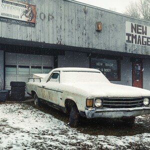 May include: A white pickup truck covered in snow is parked in front of a building with a sign that reads "NEW IMAGE PAINT & BODY INC. 828-645-7998".
