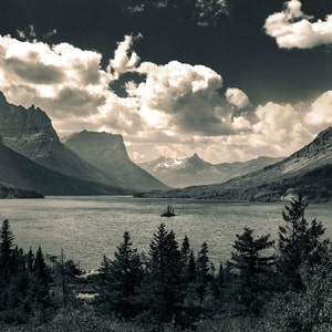 May include: A black and white photograph of a lake surrounded by mountains. The lake is calm and the mountains are covered in trees. The sky is cloudy and there is a small island in the middle of the lake.