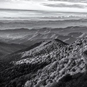 May include: A black and white photograph of a mountain range with rolling hills and a cloudy sky.