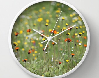 May include: White clock with a green field of orange, yellow, and white wildflowers as the background image.