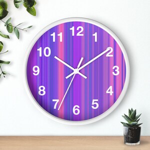 May include: A white clock with a purple and pink striped face. The clock has black hands and white numbers.