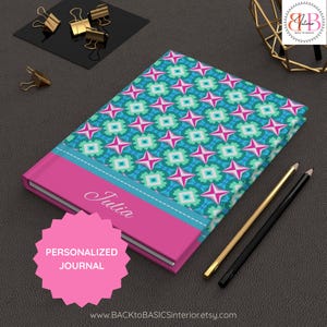 May include: A personalized journal featuring a vibrant teal and pink geometric star pattern on the cover, with a solid pink horizontal band displaying the name Julia in white script, accompanied by a gold pencil and a black pencil.