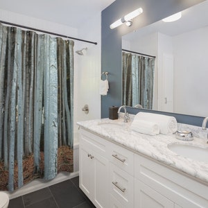 May include: A white bathroom vanity with a marble countertop and two sinks. The vanity has two drawers and two doors. A shower curtain with a forest scene is visible in the background.