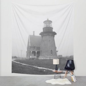 May include: Black and white photograph of a lighthouse on a foggy day. The lighthouse is a tall, brick structure with a white tower and a black roof. The lighthouse is surrounded by a grassy area and a path leading to it.