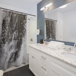 May include: A white bathroom vanity with two sinks and a marble countertop. The vanity has two drawers and two doors. The bathroom has a shower with a black and white shower curtain.