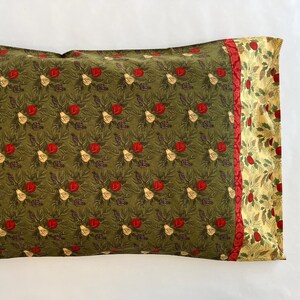May include: A rectangular pillowcase with a repeating pattern of red roses, white pears, and brown pinecones on a dark green background. A red stripe separates the main pattern from a gold floral design.