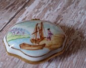 Porcelain trinket box lid decorated with C17th or early C18th settler coming ashore from sailing ship. Exotic fruits decorate the box .