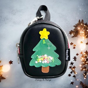 May include: A small black faux leather backpack with a zipper closure and a green felt Christmas tree applique. The tree has a yellow star on top and is decorated with white, red, and green felt embellishments. The backpack has a red and white zipper pull and a black and silver chain strap. The backpack has the text "Stringz to Things" printed on the bottom.