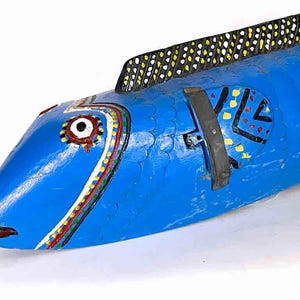 May include: A blue wooden fish sculpture with black, white, yellow, and red painted details. The fish has a large eye and a patterned design on its body.
