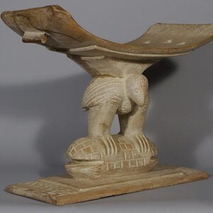 May include: A wooden stool carved in the shape of a bird with a wide, flat seat. The stool is painted white and has a detailed design.