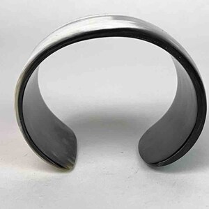 May include: A black and white horn bracelet. The bracelet is made of polished horn and has a smooth, rounded surface.