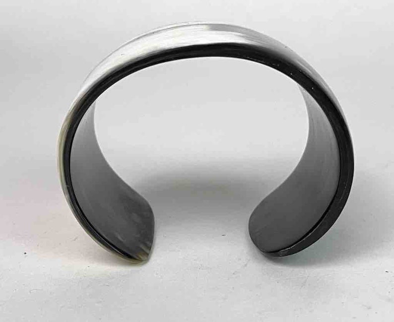 May include: A black and white horn bracelet. The bracelet is made of polished horn and has a smooth, rounded surface.