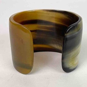 May include: A brown and black horn cuff bracelet. The bracelet is made of natural horn and has a polished finish.
