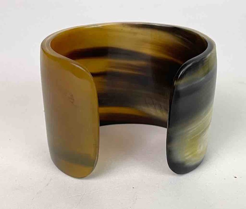 May include: A brown and black horn cuff bracelet. The bracelet is made of natural horn and has a polished finish.