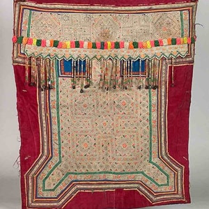 Puede incluir: Un textil de terciopelo rojo con un patrón geométrico bordado en blanco. El textil tiene una franja de cuentas azules y blancas y un ribete colorido con pequeñas flores de tela.