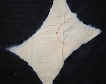 Può includere: Un pezzo di tessuto rettangolare caratterizzato da un'ampia sezione centrale color crema a forma di rombo, circondata da un bordo nero intenso. I bordi dove i colori si incontrano sono sfumati, indicando una tecnica di tintura.
