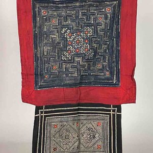 May include: A black and red textile with a geometric pattern. The textile is made of silk and has a traditional design. The textile is a square shape and has a fringe border.