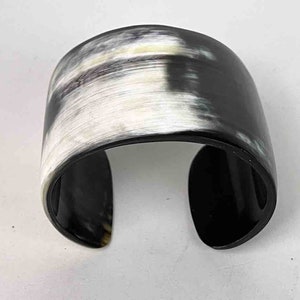 May include: A black and white horn cuff bracelet. The bracelet is made of polished horn and has a natural, organic pattern.
