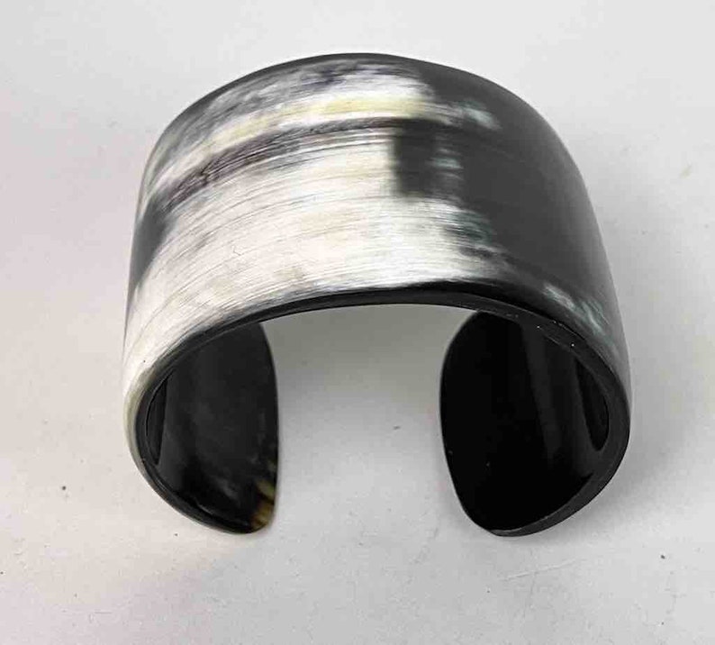 May include: A black and white horn cuff bracelet. The bracelet is made of polished horn and has a natural, organic pattern.