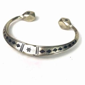 May include: A silver bracelet with a black and white geometric design. The bracelet has two rounded ends with a star design.