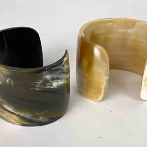 May include: Two horn bracelets, one is black and brown with a swirl pattern, the other is a light brown with a white swirl pattern.
