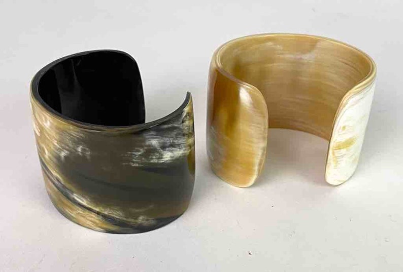 May include: Two horn bracelets, one is black and brown with a swirl pattern, the other is a light brown with a white swirl pattern.