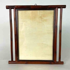 Puede incluir: Un marco de fotos rectangular de madera con un acabado marrón oscuro. El marco tiene una veta de madera natural y un respaldo de color claro. El diseño incluye soportes verticales a cada lado y una parte superior e inferior horizontales.