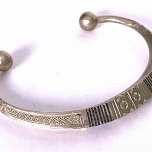 May include: A silver bangle bracelet with an intricate geometric design. The bracelet has two rounded ends.
