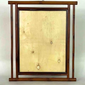 Puede incluir: Un marco rectangular de madera con un panel central de color claro. El marco está construido con madera marrón oscuro, con soportes verticales y horizontales. El panel central tiene una veta de madera clara y natural. Un pequeño gancho de metal está en la parte superior para colgar.